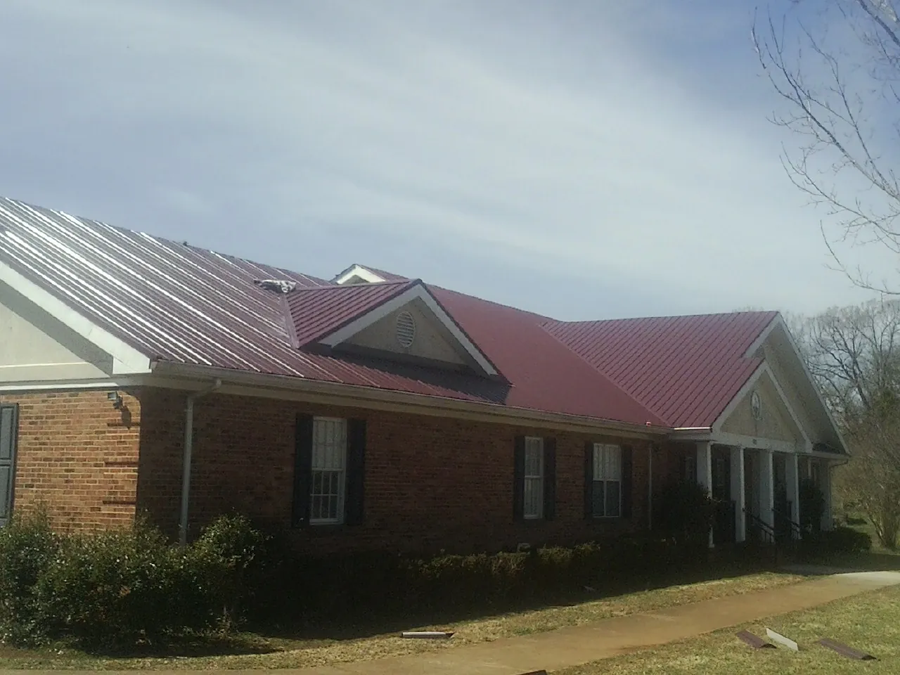 Red metal roof with gabled entries on a long brick building, from a Hail Damage Roof Repair job in Scappoose