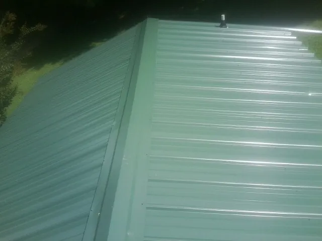 New green metal panels meeting at the ridge of a roof — Flat Roof Repair work by our crew in Scappoose