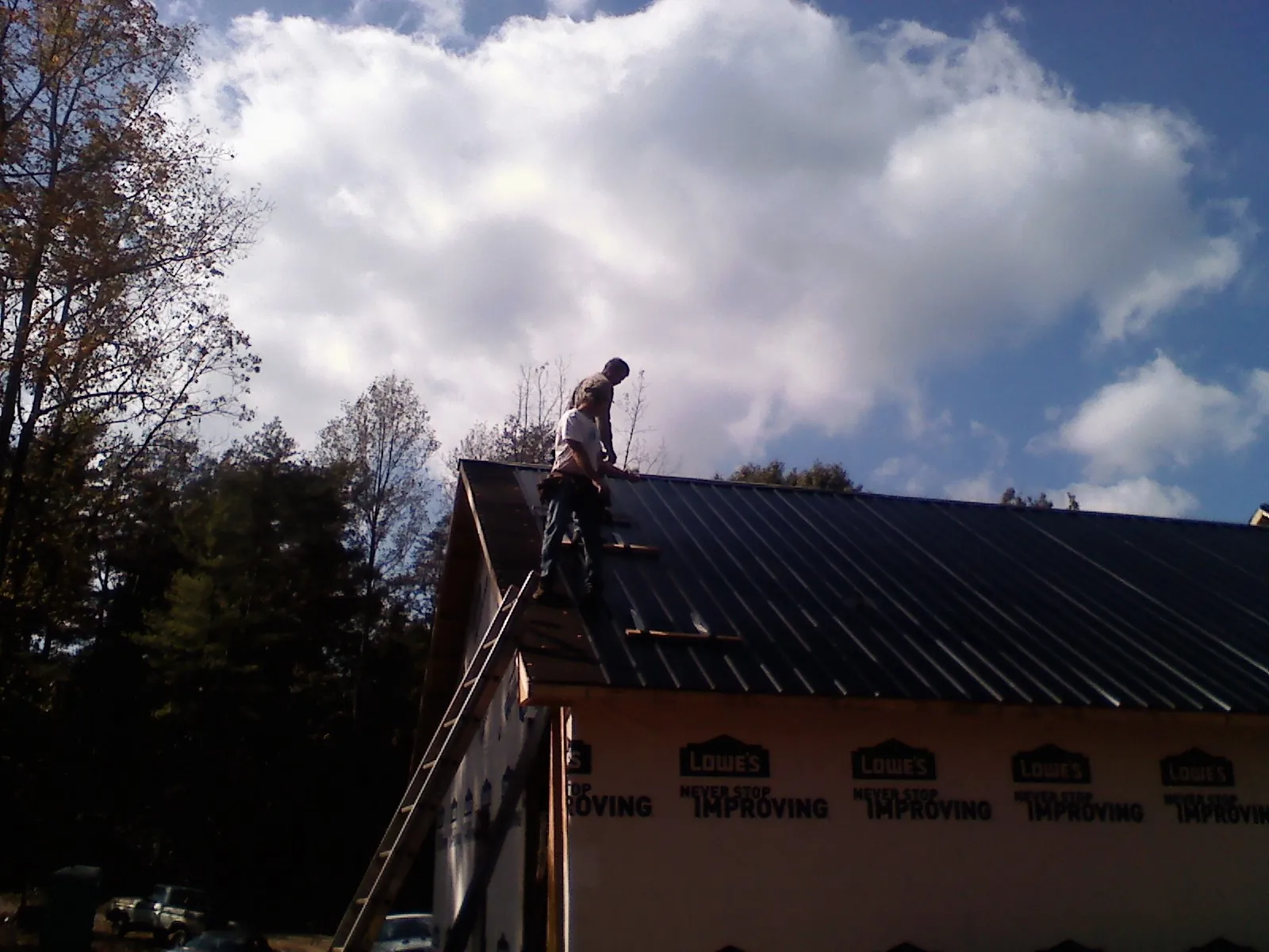 Roofer fastening dark metal panels high against a cloudy sky, from a Roof Inspection job in Scappoose