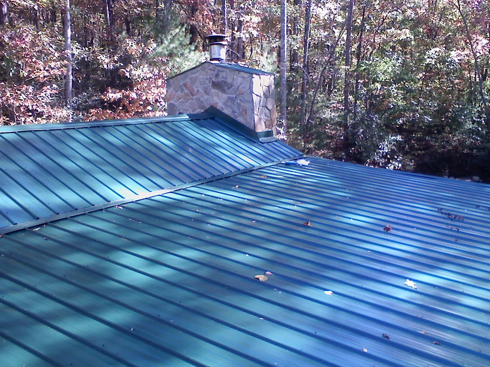 New green metal roof and stone chimney surrounded by autumn woods in Scappoose